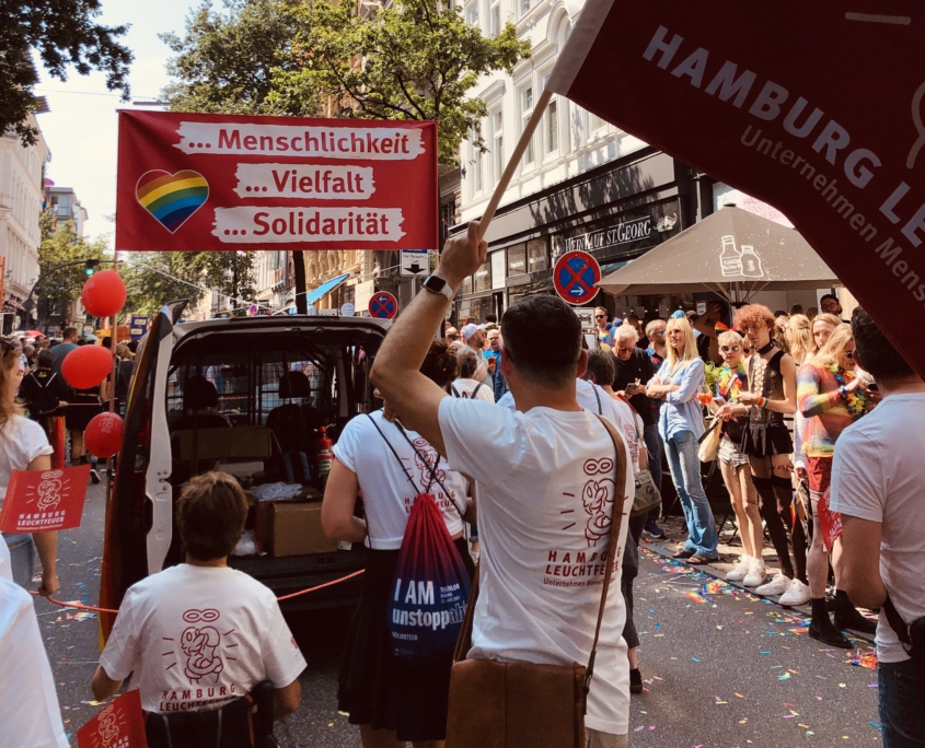 Teilnehmer*innen mit Leuchtfeuer-Fahne und im Rollstuhl beim CSD 2024.