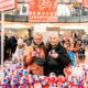 Zwei Frauen mit Teddys im Arm am Teddystand von Hamburg Leuchtfeuer, vor Ihnen aufgereit zahlreiche bunte Teddys.