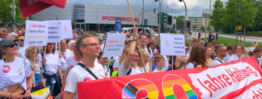 Bei der CSD Demo in Hamburg 2025 sind Mitarbeiter*innen, Ehrenamtliche und Freund*innen von Hamburg Leuchtfeuer zusammengekommen. Sie tragen ein Banner auf dem steht: "30 Jahre Haltung. Jetzt erst recht."